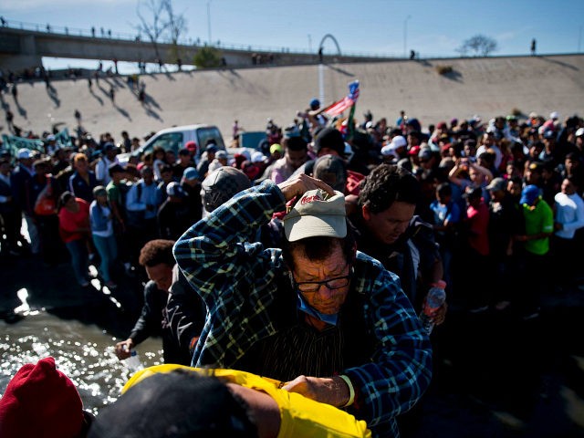 Migrants cross the river at the Mexico-U.S. border after pushing past a line of Mexican po