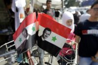 Syrians walk past Syrian national flags bearing President Bashar al-Assad's portrait in Damascus on May 11, 2014