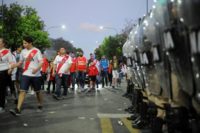 A tightly packed cordon of police holding riot shields surveys River Plate fans as they leave the Monumental stadium following the postponement of the Copa Libertadores final