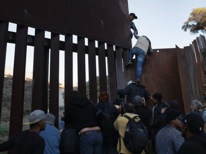 TIJUANA, MEXICO - DECEMBER 02: A woman climbs atop a fellow member of the migrant caravan