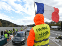 GettyImages-1070343246 A man with a sign reading 'Macron resign' waves a French flag as 'yellow vests' (Gilets jaunes) protestors gather to protest against rising oil prices and living costs at the highway's toll of La Barque, on December 9, 2018, near Marseille, southern France. - Calls mounted on December 9 for …