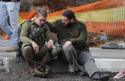 An Isreali soldier is consoled as Israeli forces and forensic experts inspect the site of a Palestinian drive-by shooting attack outside the West Bank settlement of Givat Asaf, northeast of Ramallah, on December 13, 2018. - Two Israelis were killed and at least two others were wounded at the bus …