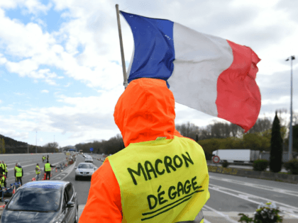 A man with a sign reading 'Macron resign' waves a French flag as 'yellow vests' (Gilets jaunes) protestors gather to protest against rising oil prices and living costs at the highway's toll of La Barque, on December 9, 2018, near Marseille, southern France. - Calls mounted on December 9 for …