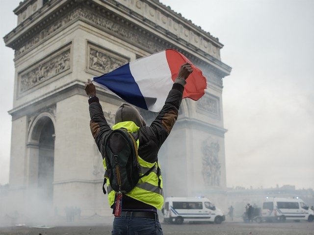 TOPSHOT - A protestor holds a french flag amid tear gas in front of the Arc de Triomphe near the Champs Elysees, in Paris on November 24, 2018 during a national rally initiated by the Yellow vests (gilets jaunes in french) to protest against rising oil prices and living costs. …