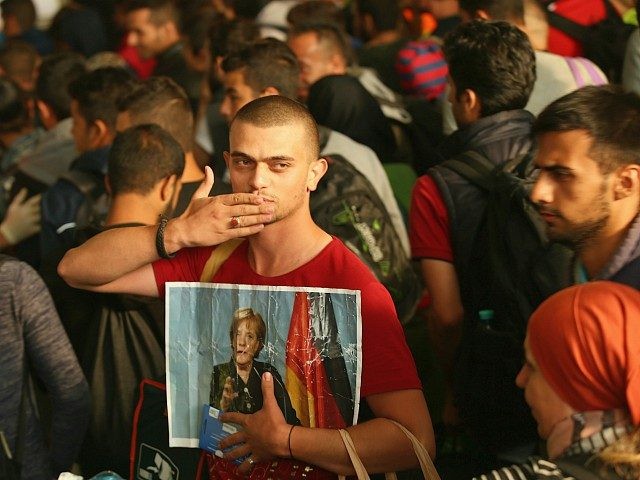 MUNICH, GERMANY - SEPTEMBER 05: A migrant from Syria holds a picture of German Chancellor Angela Merkel as he and approximately 800 others arrive from Hungary at Munich Hauptbahnhof main railway station on September 5, 2015 in Munich, Germany. Thousands of migrants are traveling to Germany following an arduous ordeal …