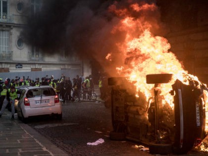 PARIS, FRANCE - DECEMBER 08: Protesters taunt police behind a burning car during the 'yell