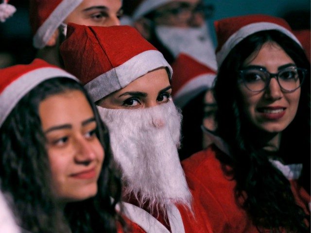 A woman dressed in a Santa Claus outfit looks on as Syrians gathered in the centre of the Syrian capital Damascus to watch the lighting of a giant Christmas tree on December 23, 2018. (Photo by LOUAI BESHARA / AFP) (Photo credit should read LOUAI BESHARA/AFP/Getty Images)