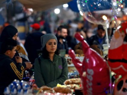 A woman sits next to a peddlar's stall in a market in the northeastern Syrian city of Qami