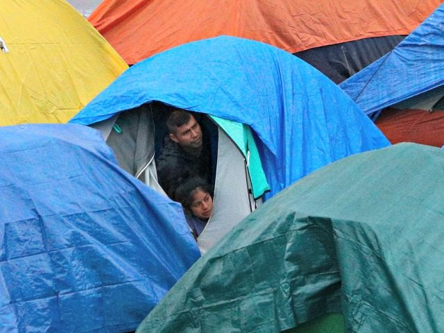 People peer from a tent at police talking with other migrants inside the Barretal migrant