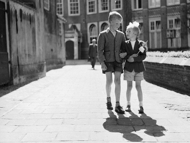 1955: A young boy and girl walking arm-in-arm along the streets of Amsterdam. The girl is holding a carnation. (Photo by Harry Kerr/BIPs/Getty Images)