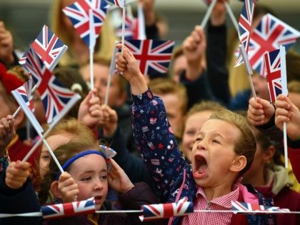 WIDNES, CHESHIRE, ENGLAND - JUNE 14: Children wave the Union Jack flag as they await the arrival of Queen Elizabeth II and Meghan, Duchess of Sussex to open the new Mersey Gateway Bridge on June 14, 2018 in the town of Widnes in Halton, Cheshire, England. Meghan Markle married Prince …