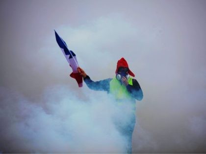 TOPSHOT - A demonstrator holds a French flag as he walks amid the tear gas during a protest of Yellow vests (Gilets jaunes) against rising oil prices and living costs, on December 1, 2018 in Paris. - Anti-government protesters torched dozens of cars and set fire to storefronts during daylong …