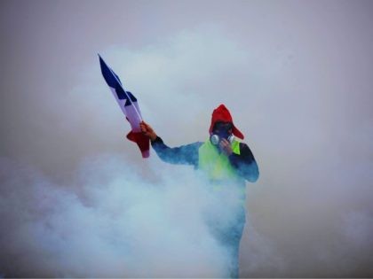 TOPSHOT - A demonstrator holds a French flag as he walks amid the tear gas during a protes