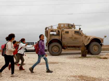 School chikldren walk past a US military vehicle in the Kurdish-held town of Al-Darbasiyah in northeastern Syria bordering Turkey on November 4, 2018. - Three armoured vehicles carrying soldiers wearing the US flag on their uniform arrived in the area after renewed tensions between Ankara and Syrian Kurds, a spokesman …