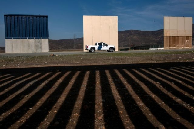 Customs and Border Protection agents drive by prototypes of a US border wall as seen from behind the Mexico-US border fence in Tijuana, Mexico