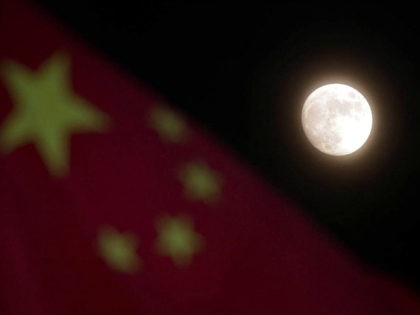 The moon is seen near a Chinese national flag in Beijing Sunday, Dec. 15, 2013. China's first moon rover touched the lunar surface and left deep traces on its loose soil, state media reported Sunday, several hours after the country successfully carried out the world's first soft landing of a …
