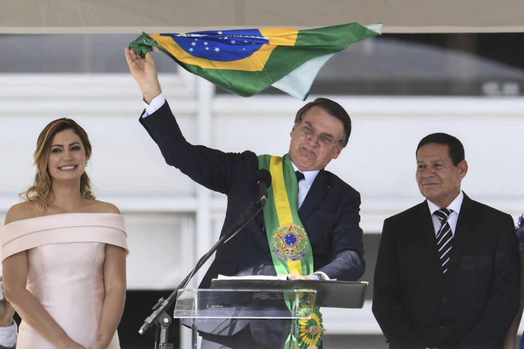 Brazil's new President Jair Bolsonaro (C) waves a national flag while addressing supporters flanked by First Lady Michelle Bolsonaro (L) and Brazil's new Vice-President Hamilton Mourao, during their inauguration ceremony