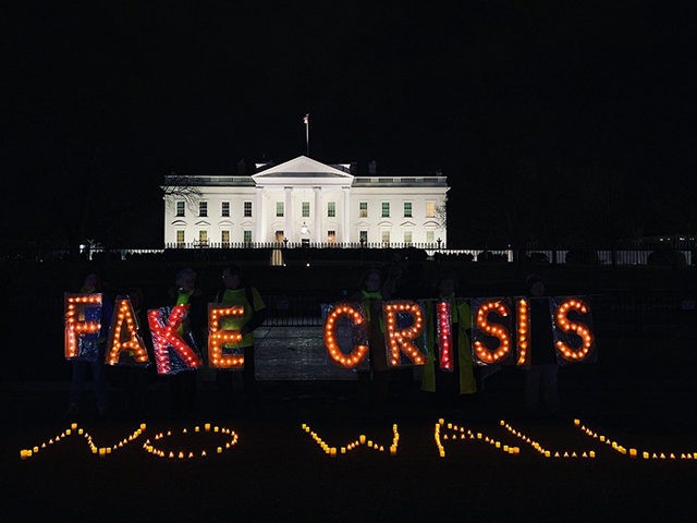 Protesters hold up lights reading "FAKE CRISIS" behind lights arranged on the ground readi