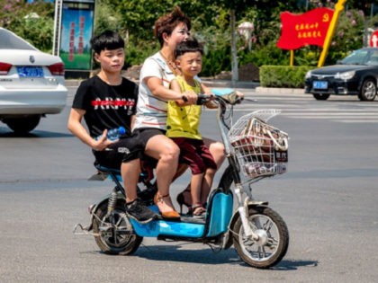 A woman rides her scooter with two children in Huaxian county in China's central Henan province on August 28, 2018. - China's moves to combat an ageing population by relaxing decades-old curbs on family size have hit an unexpected snag: many parents are no longer interested in having more babies.