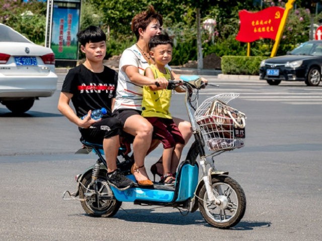 A woman rides her scooter with two children in Huaxian county in China's central Henan pro