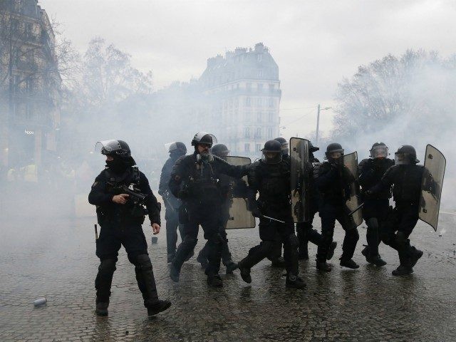 Police officers walk amidst the teargas after firing it during a demonstration by yellow v