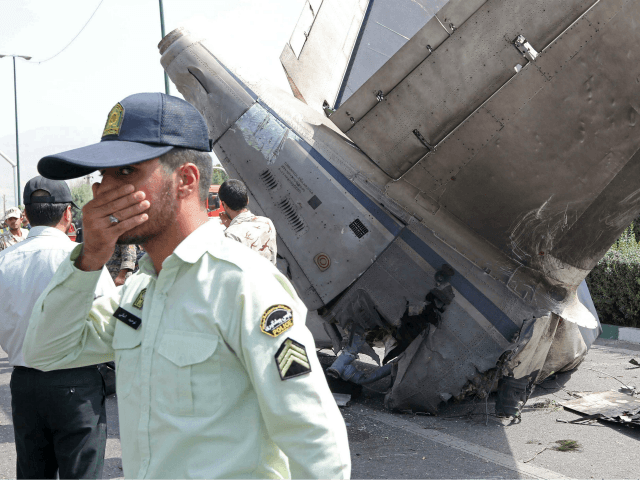 Iranian security forces stand next to the remains of a plane as they secure the scene of a