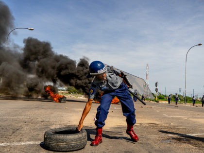 TOPSHOT - A police officer removes tyres set by protesters during a 'stay-away' demonstration against the doubling of fuel prices on January 14, 2019 in Emakhandeni township, Bulawayo. - Zimbabwe's President on January 12 announced a more than 100 percent rise in the price of petrol and diesel in a …