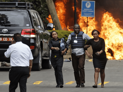 Security forces help civilians flee the scene as cars burn behind, at a hotel complex in N