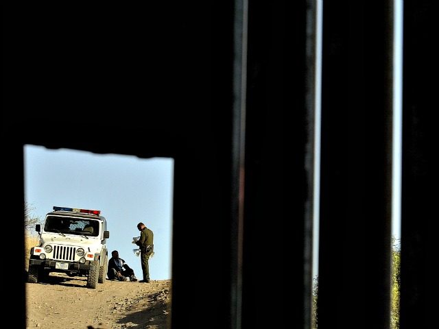 A U.S. Border Patrol agent questions a man in Nogales, Ariz., seen through a hole in a met