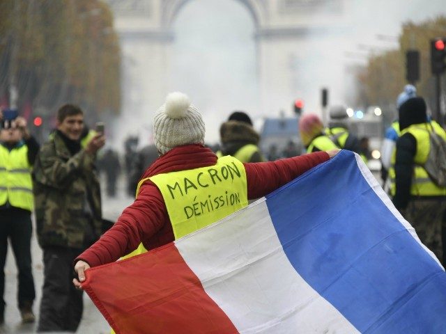 A woman wears a Yellow vest (Gilet jaune) reading "Macron resign" on the Champs