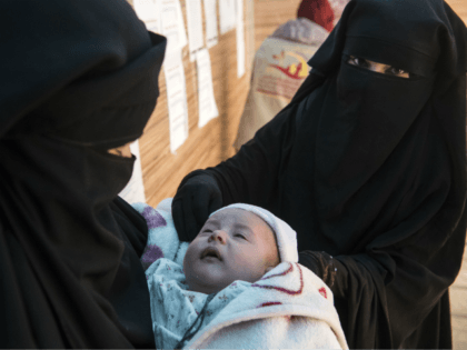 Displaced Syrian women hold a child as they wait at a makeshift clinic at the Internally D