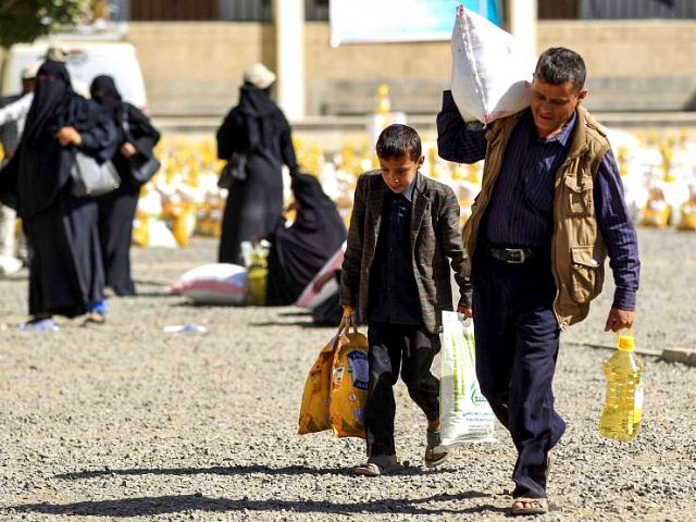 A Yemeni man and boy walk carrying bags of food aid provided by a local charity to familie
