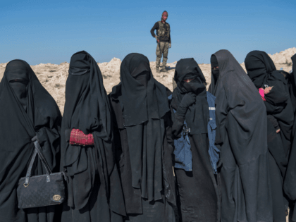 TOPSHOT - A fighter with the US-backed Syrian Democratic Forces (SDF) keeps watch near veiled women standing on a field after they fled from the Baghouz area in the eastern Syrian province of Deir Ezzor on February 12, 2019 during an operation to expel hundreds of Islamic State group (IS) …