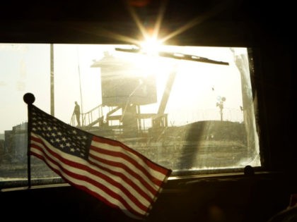 A border guard stands on Iraq's border with Kuwait behind a US flag fluttering on the dashboard of a Mine Resistant Ambush Protected (MRAP) vehicle from the 3rd Brigade Combat Team, 1st Cavalry Division as the last US convoy leaves Iraq on December 18, 2011.