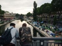 TOPSHOT - Men look at a makeshift camp during its evacuation by police, along the Canal de Saint-Martin at Quai de Valmy in Paris, on June 4, 2018. - More than 500 migrants and refugees were evacuated on early June 4, 2018 from a makeshift camp that had been set …