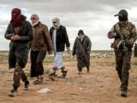 Men suspected of being an Islamic State (IS) group's fighter walk next to a member of the Kurdish-led Syrian Democratic Forces (SDF) as they wait to be searched after leaving the IS group's last holdout of Baghouz, in Syria's northern Deir Ezzor province on February 27, 2019.