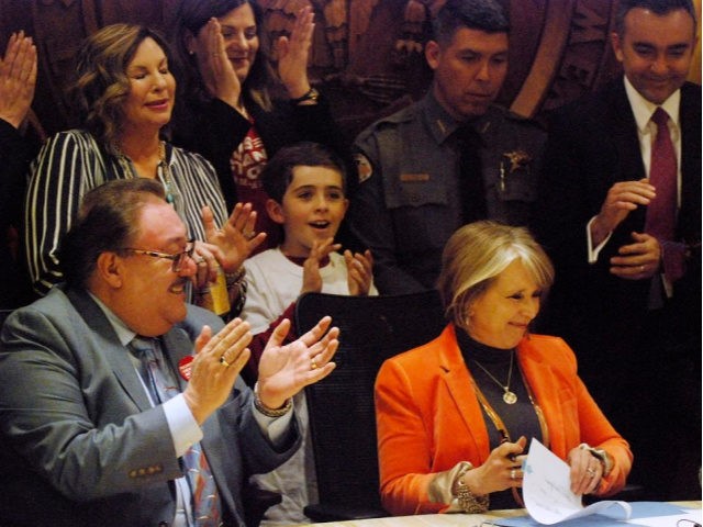 Democratic New Mexico Gov. Michelle Lujan Grisham, sitting right, signs a bill into law that expands background checks to nearly all gun sales in New Mexico in a ceremony in in Santa Fe, N.M., Friday, March 8, 2019.