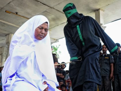 A crowd watch an unidentified 'punk' Indonesian female (L), who was caught having pre-marital sex in public with a male partner, being caned by a sharia police officer dressed in black robes at a public square in Langsa town on April 20, 2012. The homeless 'punk' couple in their early …