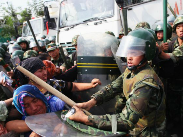 Chinese policemen push Uyghur women protesting on the streets of Urumqi, the capital of Xi