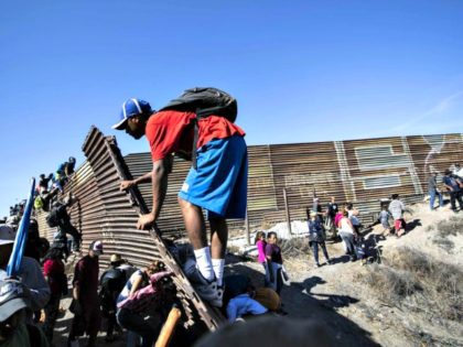 A group of Central American migrants -- mostly Hondurans -- climb a metal barrier on the U