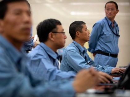 Workers sit at computer terminals as they monitor a large display screen in the command ce