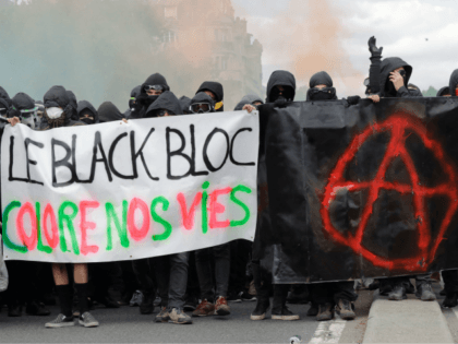 Protestors dressed in black and with the face covered hold smoke bombs and a banner reading 'The Black bloc colours our lives' and depicting the Anarchist symbol as they take part in a march for the annual May Day workers' rally, in Paris, on May 1, 2018. (Photo by Thomas …