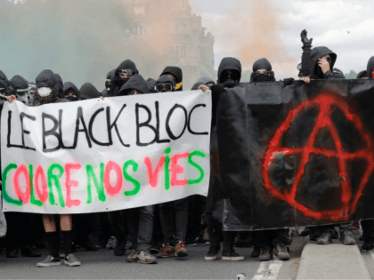 Protestors dressed in black and with the face covered hold smoke bombs and a banner readin