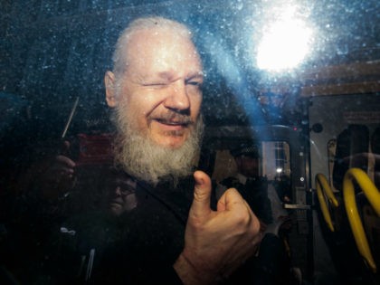 Julian Assange gestures to the media from a police vehicle on his arrival at Westminster M