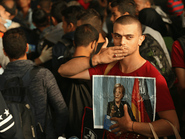 MUNICH, GERMANY - SEPTEMBER 05: A migrant from Syria holds a picture of German Chancellor Angela Merkel as he and approximately 800 others arrive from Hungary at Munich Hauptbahnhof main railway station on September 5, 2015 in Munich, Germany. Thousands of migrants are traveling to Germany following an arduous ordeal …