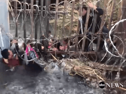 Video published by ABC News shows migrants pushing children under a fence in a water-fille