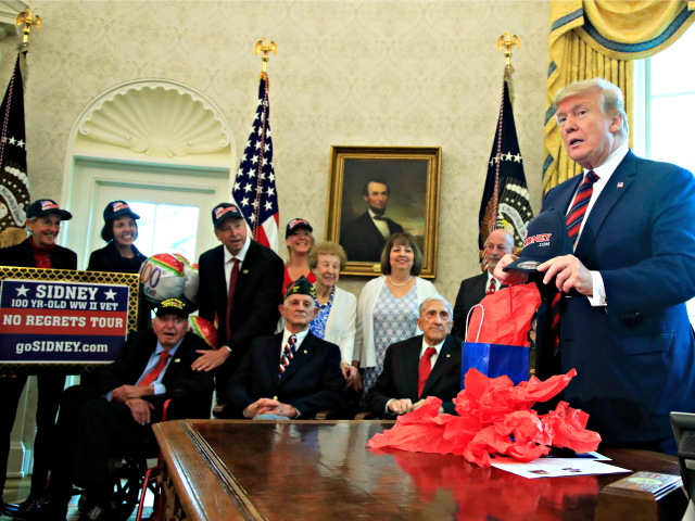 President Donald Trump is presented with a cap by World War II veterans, seated from left,