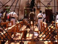 Sri Lankan security personnel walk past debris next to a dead body slumped over a bench following an explosion in St Sebastian's Church in Negombo, north of the capital Colombo, on April 21, 2019. - A series of eight devastating bomb blasts ripped through high-end hotels and churches holding Easter …