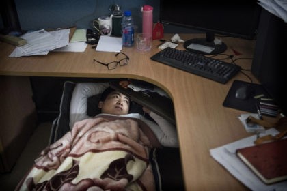 SHENZHEN, CHINA - APRIL 12: A Huawei employee watches a program on his smartphone as he rests at his cubicle during lunch break, which is known to be common practice in many workplaces in China, at the research and development area in the Bantian campus on April 12, 2019, in …