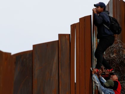 A Honduran migrant is boosted up by two friends as he jumps the U.S. border wall to surren